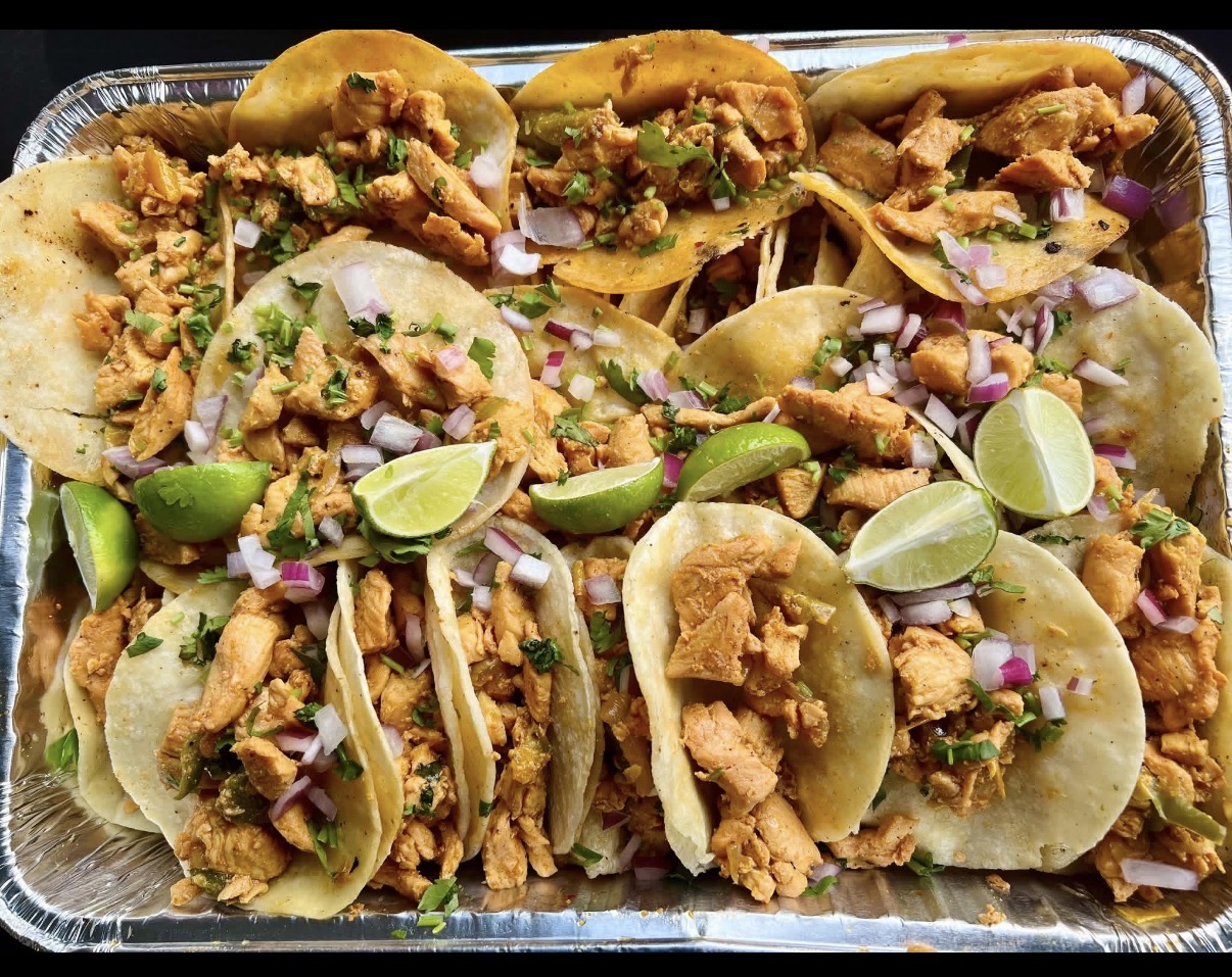 Stainless steel catering trays loaded with hand-pressed tortillas, asada, pastor, and chicken